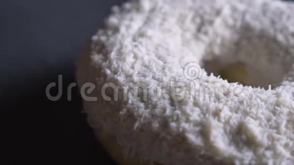在灰色的桌子背景下用椰子片慢慢旋转的美味的白色甜甜圈特写镜头视频的预览图