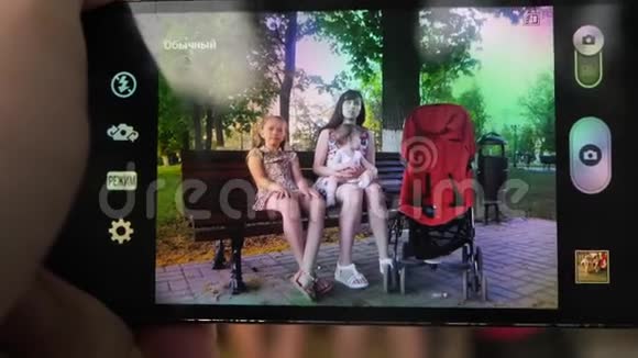 许多孩子的母亲和她的孩子坐在公园的长凳上打着电话微笑着看着视频的预览图