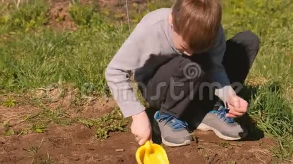 男孩用黄色塑料铲子在房子附近的草坪上挖地视频的预览图