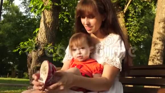 妈妈鞋童鞋坐在夏天公园的长凳上微笑着慢动作视频的预览图