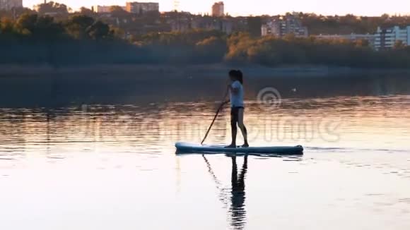 长镜头美丽的女孩与船帆站在河上的苏普视频的预览图