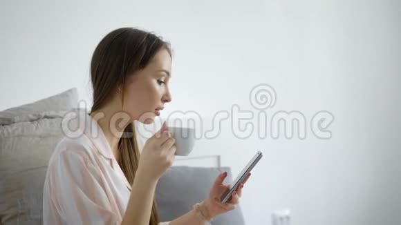 一位美女手里拿着一个杯子和一部智能手机的肖像一位女士看着一个小玩意上的新闻喝着茶视频的预览图