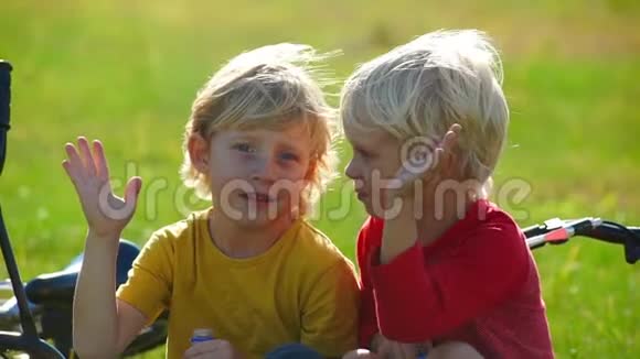 两个小男孩骑自行车的慢动作镜头坐在草坪上给对方五个成功的概念友谊视频的预览图