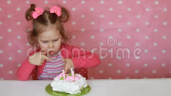 一个有趣的小女孩吃了一个美味的蛋糕一个孩子在粉红色背景的桌子上吃甜点视频的预览图
