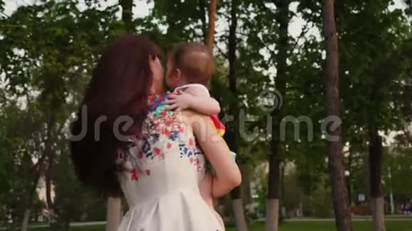 年轻的母亲在怀里抱着一个婴儿笑着和他一起在城里散步视频的预览图