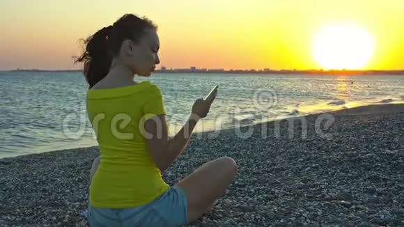 日落时拿着电话在海滩上的女孩视频的预览图