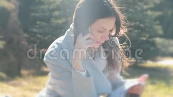 布尼斯女人坐在春天公园的草地上用手机说话的肖像视频的预览图