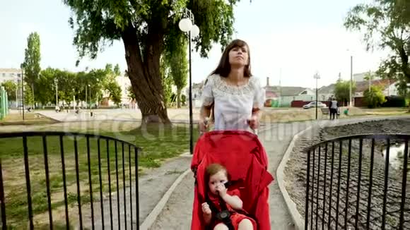 带着小孩的女人在夏天的公园里散步带着婴儿车穿过池塘的桥慢动作视频的预览图