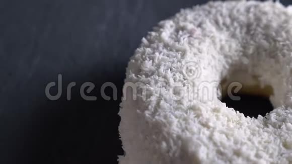 在灰色的桌子背景上用椰子片慢慢旋转的美味白甜甜圈的特写镜头视频的预览图