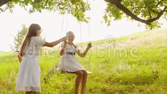 快乐的孩子们在一棵夏天的橡树下荡秋千笑起来少女在大自然中嬉戏微笑视频的预览图