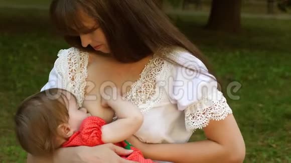 小宝宝从妈妈的乳房里吸奶妈妈正在给孩子喂奶坐在公园的长椅上微笑视频的预览图