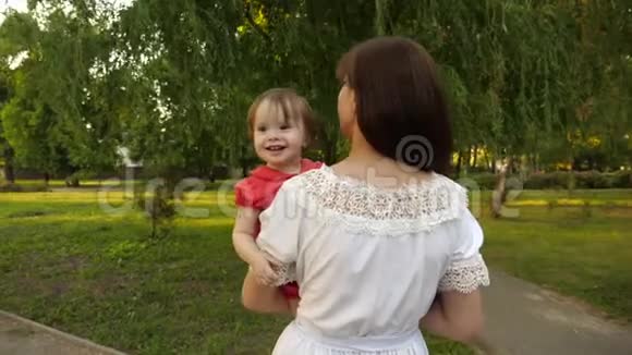 快乐的宝宝微笑着坐在妈妈的怀里在夏天的公园里展示手指慢动作视频的预览图