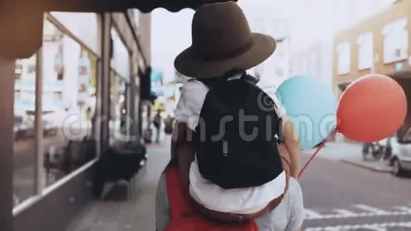 妈妈肩膀上男孩两个气球母亲和儿子带着背包一起沿着街走4K视频的预览图