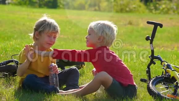 两个小男孩骑自行车的慢镜头坐在草坪上给对方五个成功的概念友谊视频的预览图