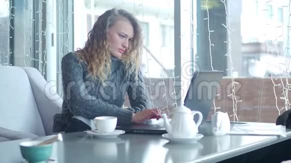 女士用手提电脑工作触摸头发在咖啡馆里寻找视频的预览图