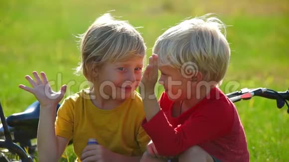 两个小男孩骑自行车的慢动作镜头坐在草坪上给对方五个成功的概念友谊视频的预览图