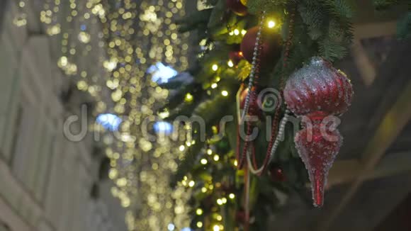 挂在云杉树枝上的红色圣诞玩具在背景中失去焦点的是黄色的节日照明视频的预览图