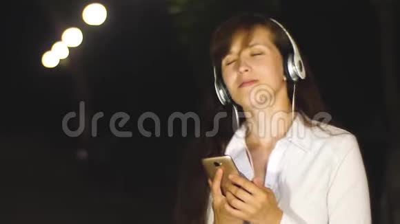 年轻女孩戴着耳机手提电话跳舞微笑着唱歌晚上音乐让人肾上腺素激增视频的预览图