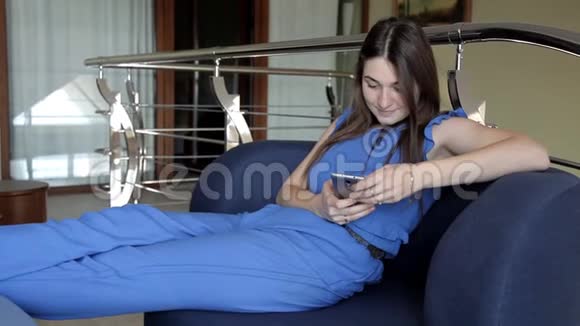 一个年轻女孩坐在沙发上打电话看短信视频的预览图