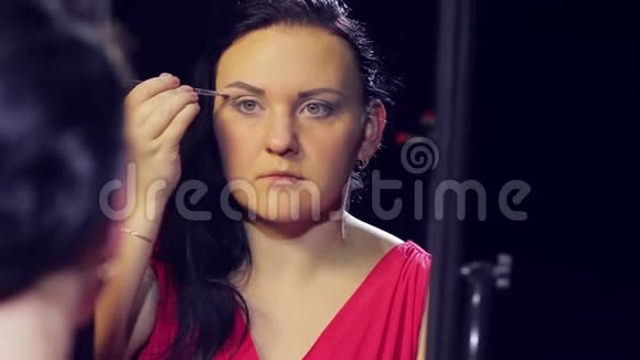 一个年轻的黑发女人穿着一件红色的裙子在镜子前用画笔用浅色的色调化妆视频的预览图