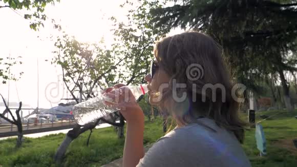 漂亮的小女孩在公园户外的塑料瓶里喝水不受阳光的照射视频的预览图