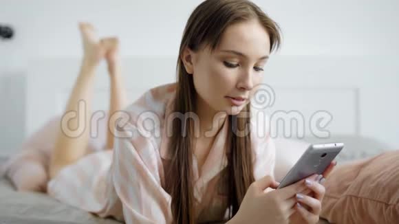 年轻的女人手里拿着手机在卧室里女士早上用手机说话她看起来很开心视频的预览图