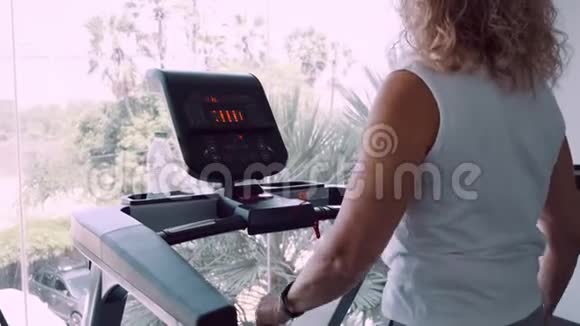 在全景窗口背景下老年妇女在健身房的跑步机上订婚视频的预览图