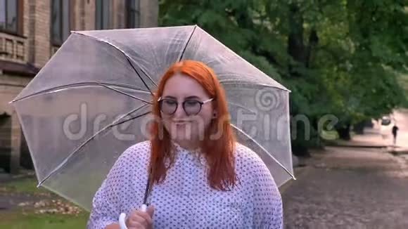 戴眼镜的胖姜女孩在雨天的公园里散步撑着伞思考着概念视频的预览图