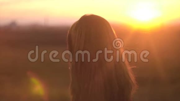 美丽的长发女人的肖像背景是夕阳的阳光头发飘动的迷人女子视频的预览图