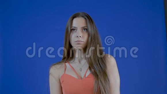 一个年轻迷人的女孩的肖像长发在工作室的蓝色背景上慢动作视频的预览图