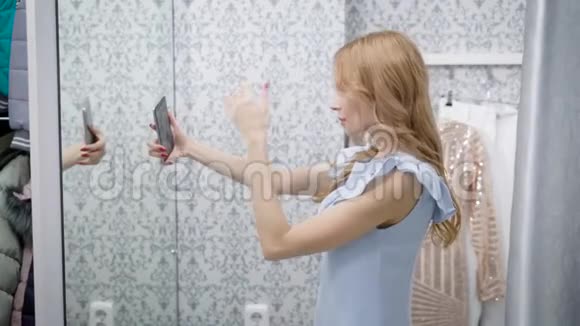 年轻女子正在用智能手机在服装店试衣间的镜子里拍照视频的预览图
