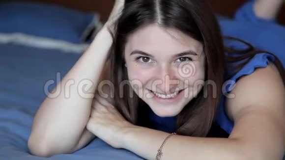年轻女孩躺在蓝色的床上对着镜头摆姿势视频的预览图