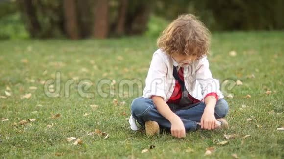 悲伤的卷曲男孩在草地上聊天他低头低下头然后他会抬起眼睛看着摄像机视频的预览图