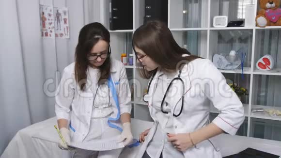 两位漂亮的年轻医生女士用纸质文件双人核对档案两名女医生在检查室里视频的预览图