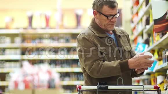戴眼镜的成熟男人在超市的货架上挑选商品把罐子放在购物车里视频的预览图
