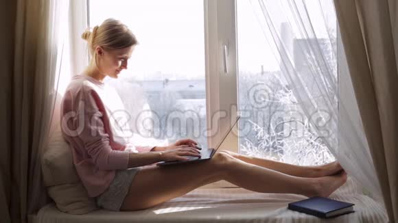 坐在窗台上用笔记本电脑工作的女人冬季天气晴朗视频的预览图