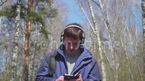 一个年轻人走在公园里通过耳机听音乐早晨在春天的新鲜空气中散步视频的预览图