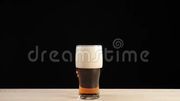 新鲜啤酒手从黑色背景的木桌上拿出一杯啤酒杯中的美味工艺啤酒冷鲜啤酒视频的预览图