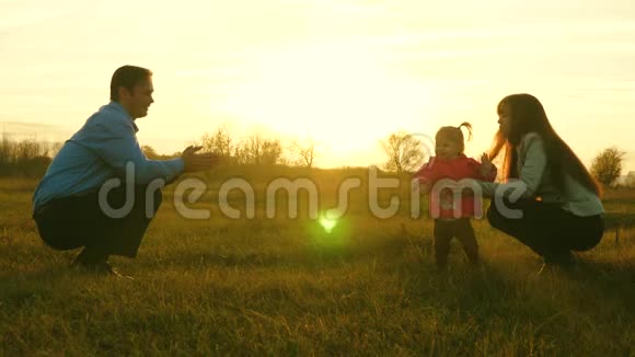 爸爸妈妈和孩子在日落时在草地上玩家庭幸福的概念宝宝从爸爸到妈妈都在草坪上儿童视频的预览图