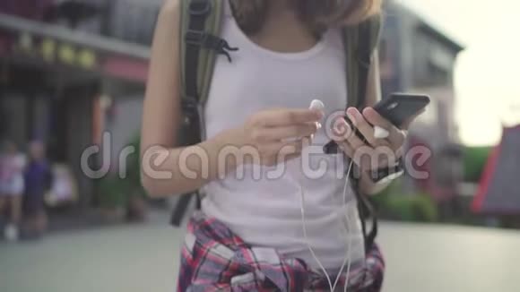 亚洲背包客博主女性使用智能手机聊天查看社交媒体在唐人街旅游时听音乐视频的预览图