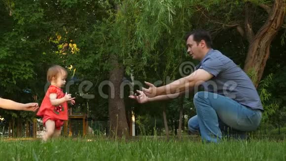 小女儿迈出第一步在公园的草坪上遇见笑着的爸爸爸爸亲吻婴儿的脸颊和微笑慢慢视频的预览图