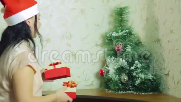 一个戴着圣诞老人帽子的微笑女人正在圣诞树下放圣诞礼物视频的预览图