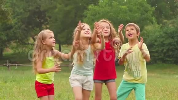 快乐的孩子男孩和三个女孩在夏天的草坪上玩肥皂泡慢动作视频的预览图