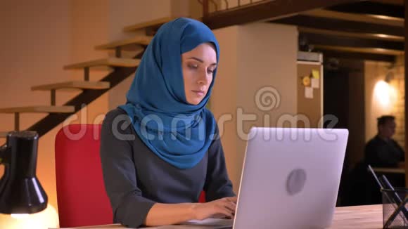 年轻漂亮的阿拉伯女办公室职员在笔记本电脑上打字看着相机微笑着的特写照片视频的预览图