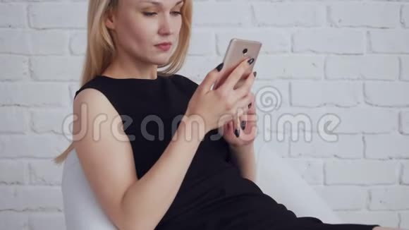 年轻迷人的女人穿着黑色连衣裙看着智能手机视频的预览图