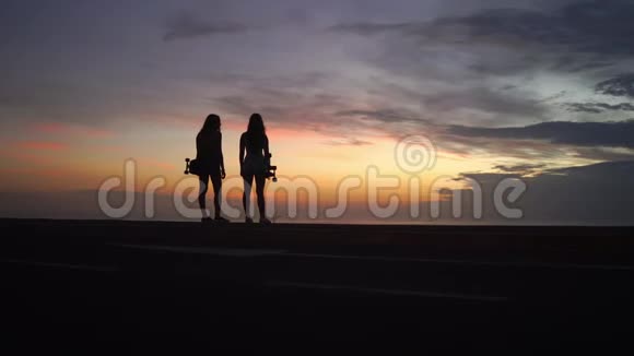 两个女孩站在路边手里拿着滑板看日落视频的预览图