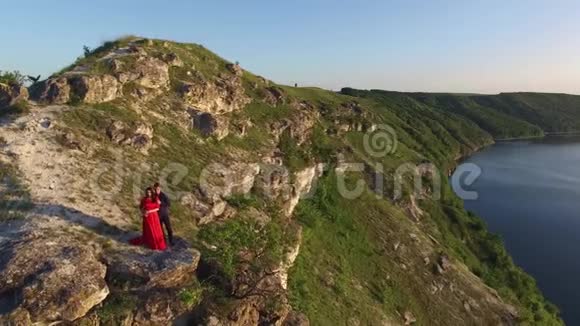 空中飞行远离相爱的情侣站在水边的悬崖边穿着漂亮红裙子的女人一个黑人视频的预览图