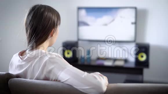 年轻女子坐在客厅的沙发上看电视她热衷于电影电影惊悚片视频的预览图