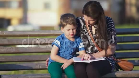 年轻的母子坐在公园的长凳上看书视频的预览图