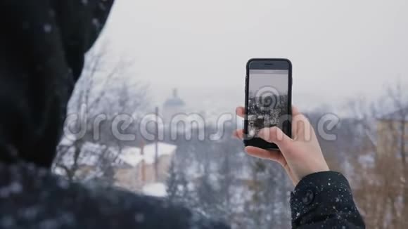 穿着黑色引擎盖的人使用电话显示了老城区和白雪皑皑的冬季公园的美景慢动作视频的预览图